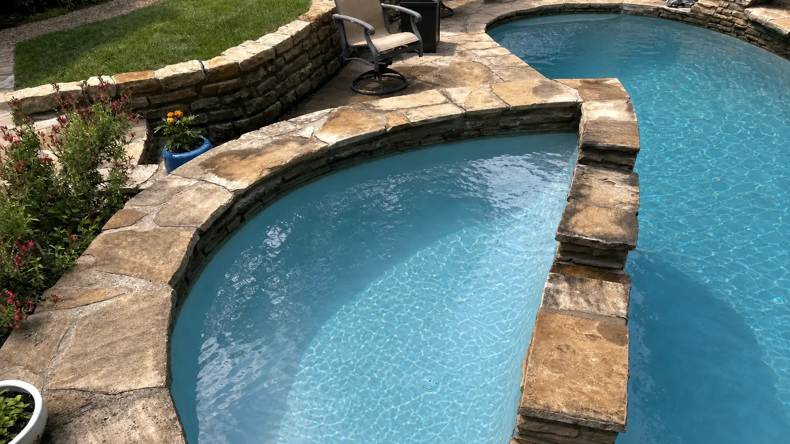 A clean freeform pool with a raised stone spa and flagstone coping in a landscaped backyard.