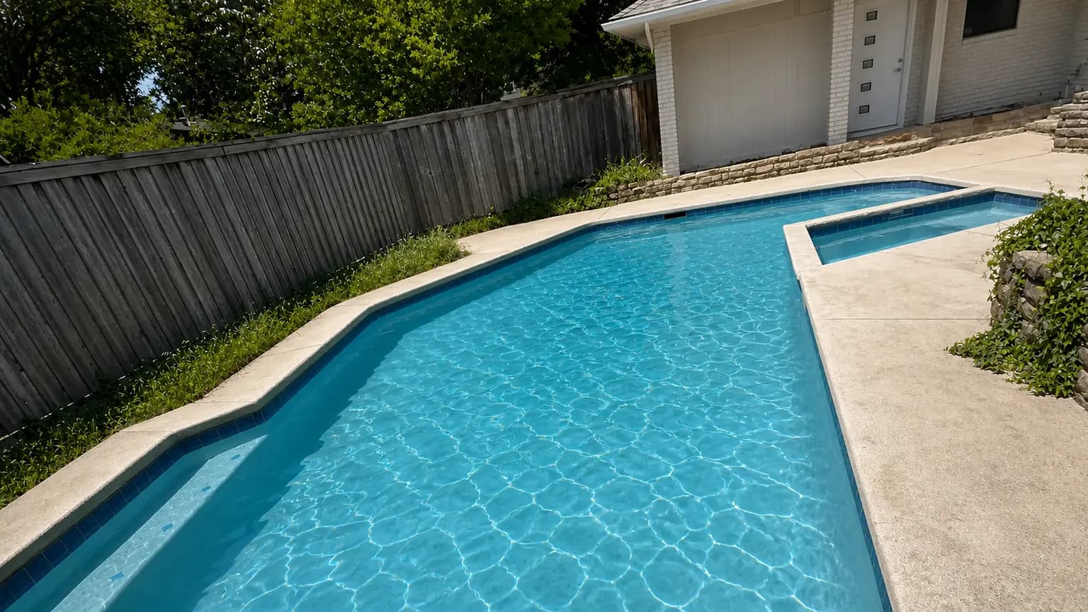 A clean backyard pool with an attached spa, bordered by a wood privacy fence along the property line.